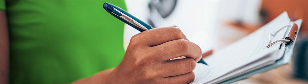 Frau schreibt mit einem Stift von Hand auf das Klemmbrett. (Bildnachweis: iStock.com/VioletaStoimenova)